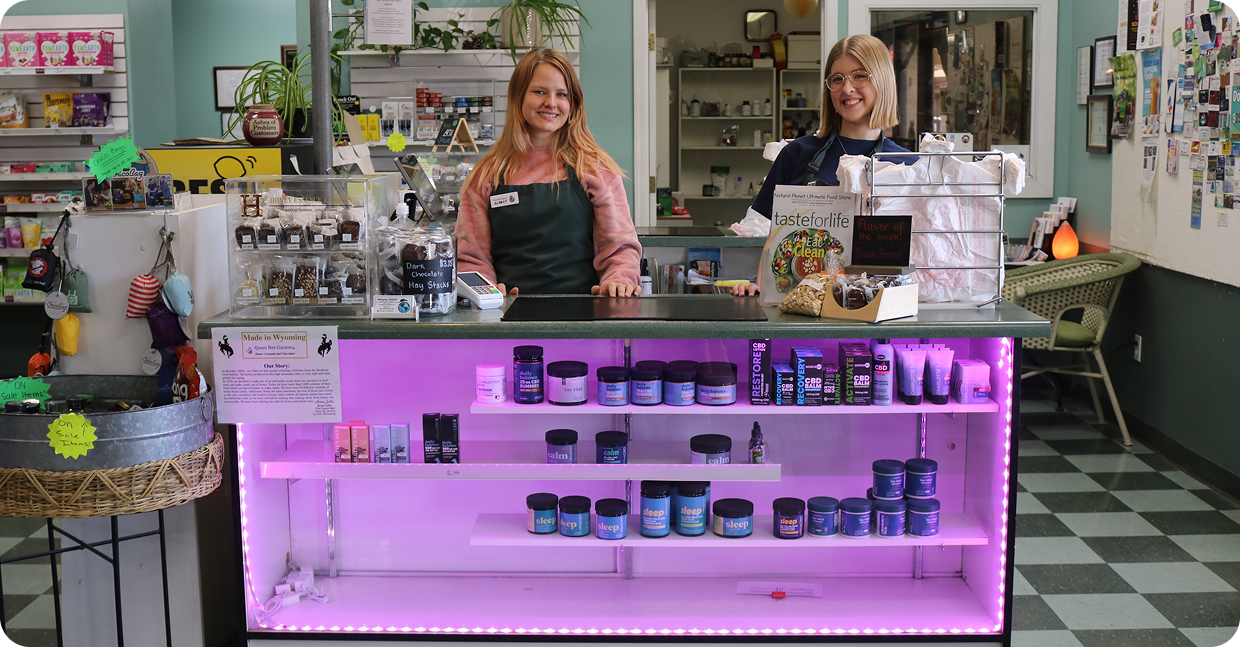 Two women smiling behind a counter with skincare products and glowing purple lights.